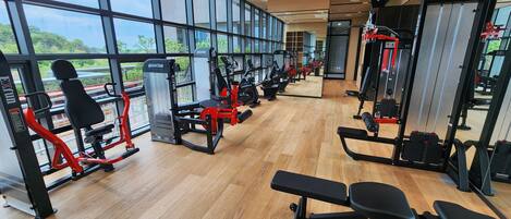 A gym with various exercise equipment, large windows, and a wooden floor.