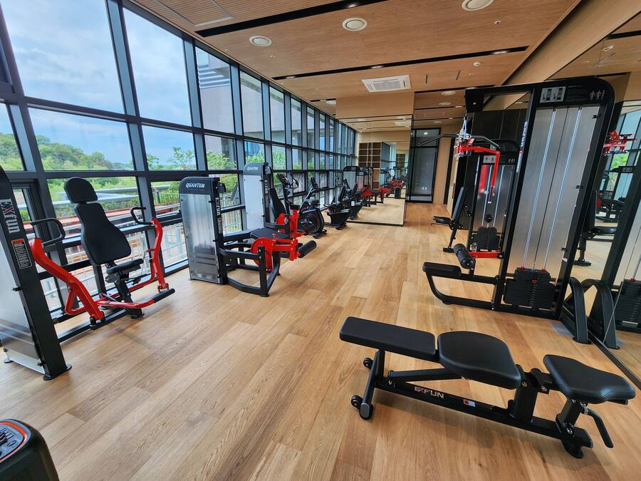 A gym with various exercise equipment, large windows, and a wooden floor.