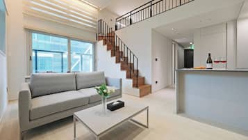 Una sala de estar moderna con un sofá gris, una mesa de centro con un florero y una escalera con escalones de madera y barandillas negras.