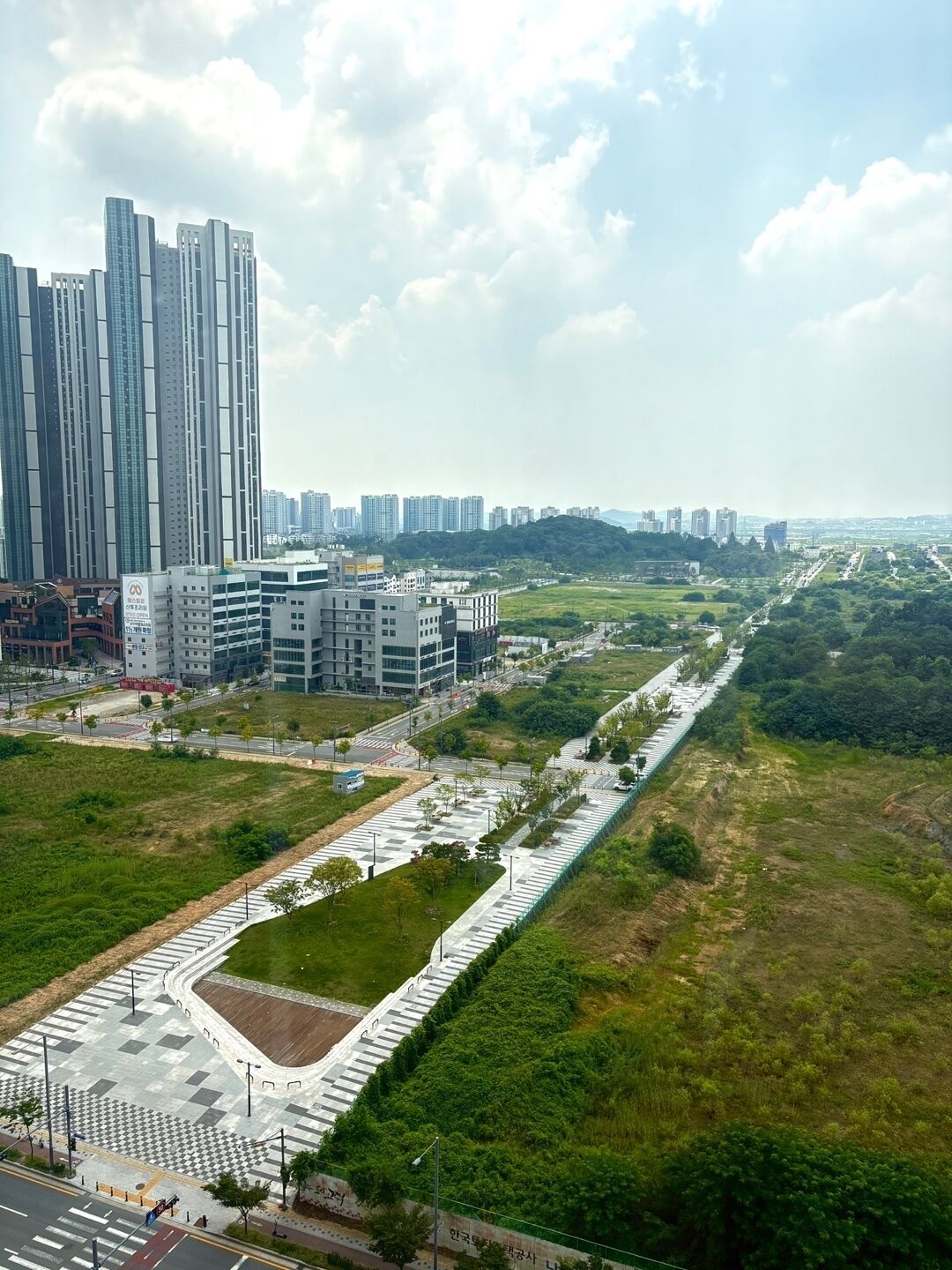 Un complejo de edificios altos con arquitectura moderna, un amplio espacio peatonal con diseño a cuadros y una zona verde con parque.