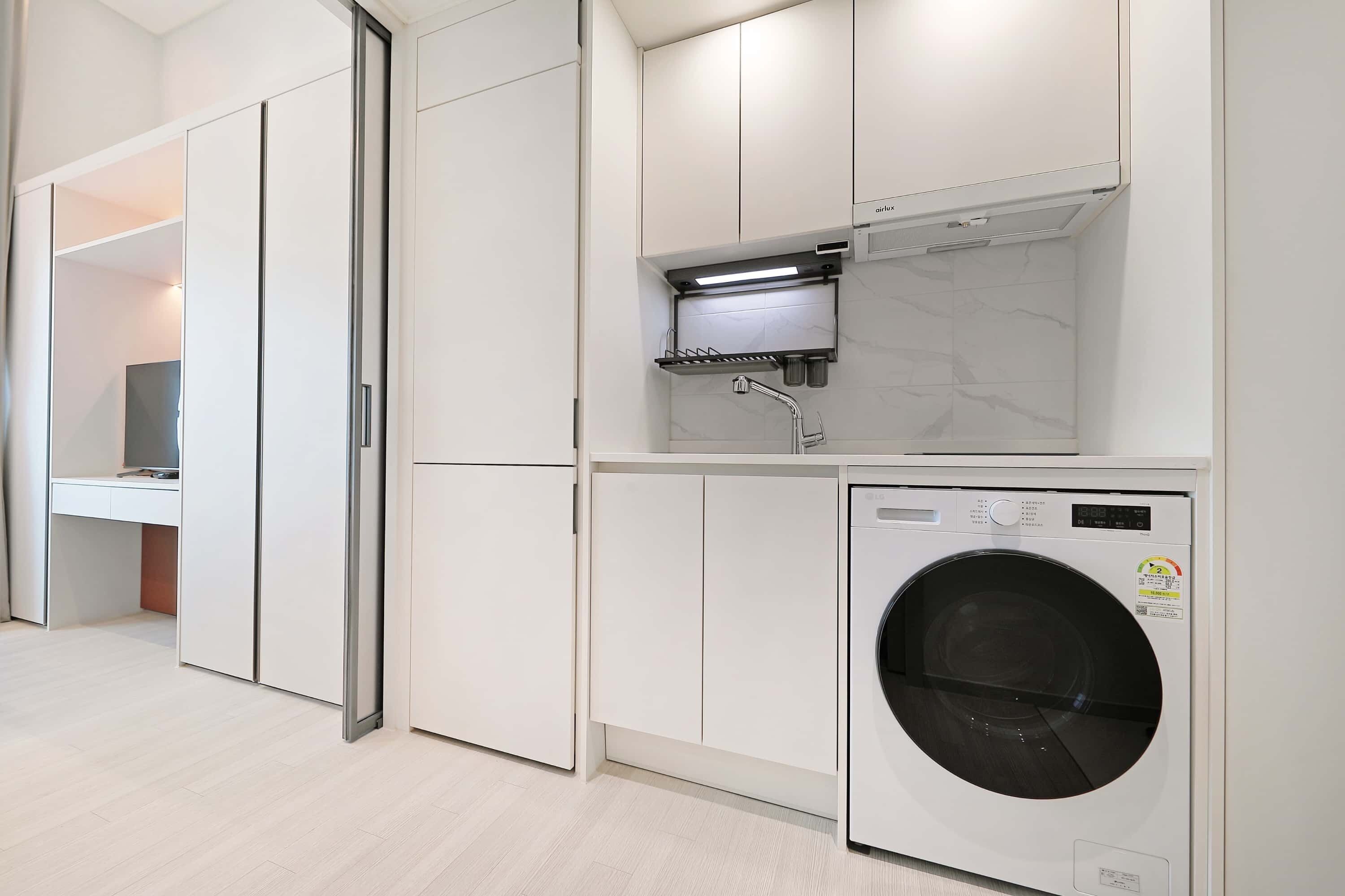 Een moderne wasserij met een voorlader wasmachine, een inbouw droger en een klein plankje boven de droger.