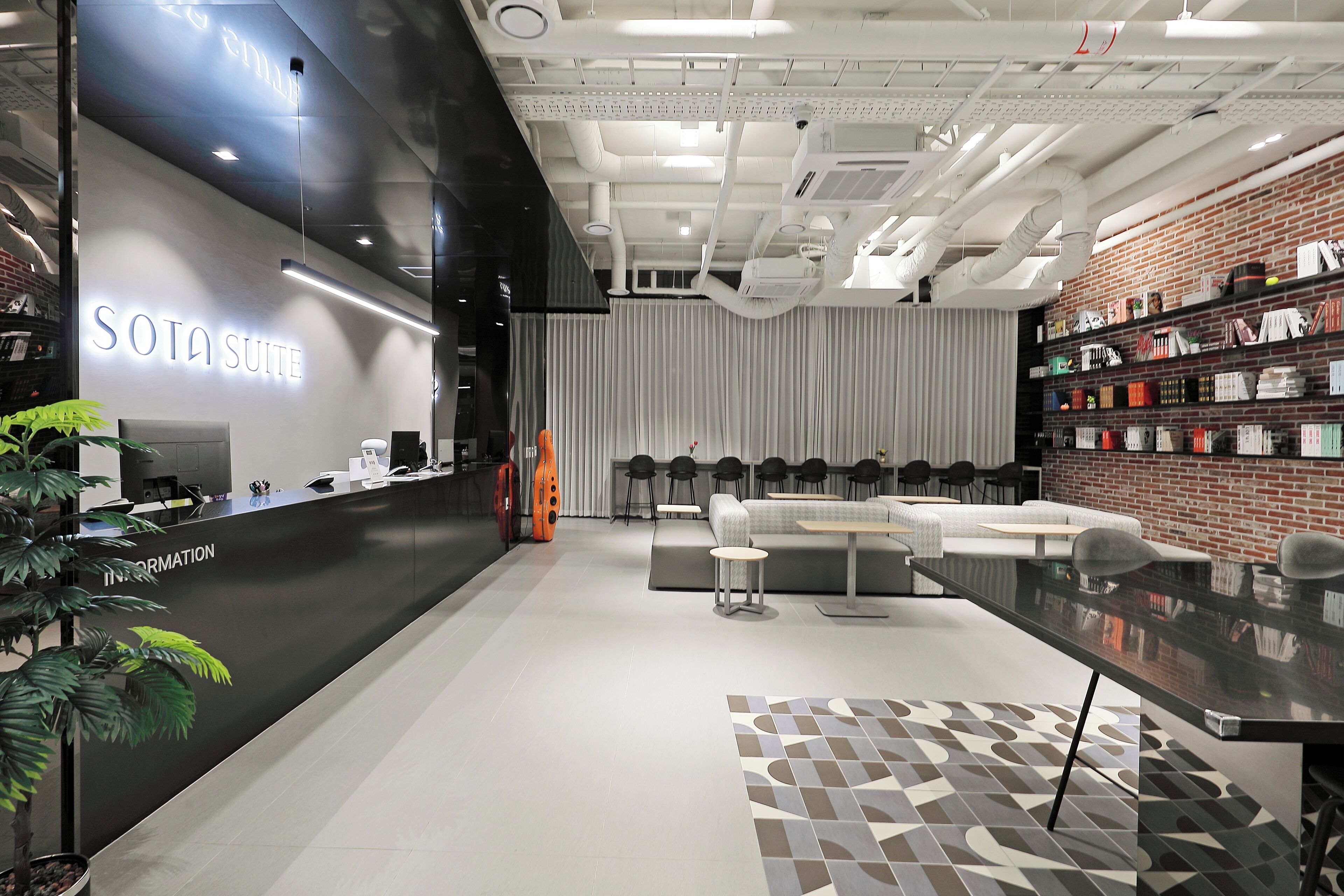En modern hotellobby med en receptionsdisk märkt "SOTA SUITE", en sittgrupp med soffor och fåtöljer samt en utställning med olika föremål på hyllor.