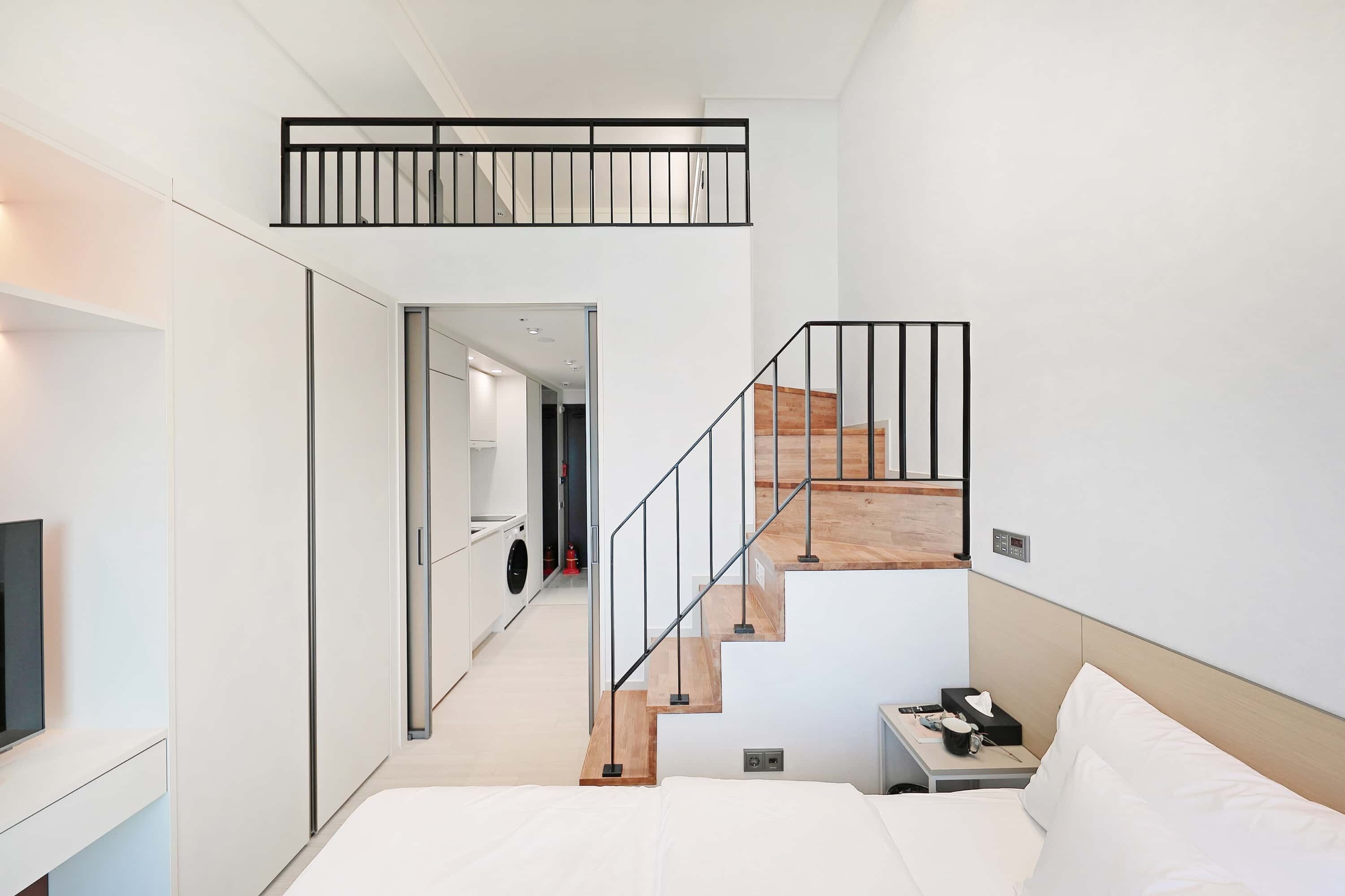Quarto de hotel moderno com uma cama, escrivaninha, televisão e escada para um andar superior.