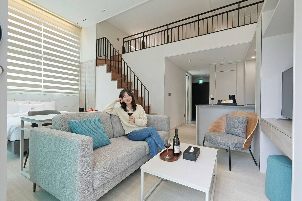 Un salon moderne avec un canapé, une table basse et un fauteuil. Un escalier mène à un niveau supérieur.