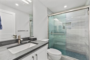 Une salle de bain moderne avec une douche à parois de verre, des toilettes blanches et un meuble-lavabo à deux vasques.