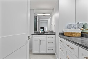 Une salle de bain moderne avec des meubles blancs, un plan de travail noir et un miroir.