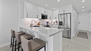 A modern kitchen with white cabinetry, stainless steel appliances, and a central island with bar stools.