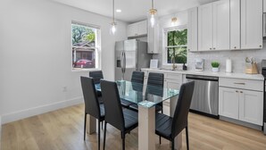 A modern kitchen with white cabinets, stainless steel appliances, and a glass dining table with black chairs. - Carolina Cottage Near Ft Jackson, 5Pts & Zoo! Sleeps 12-Spacious 4 bed/2.5 bath! (Columbia)
