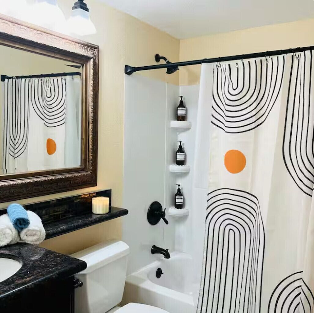 Een badkamer met een douche, toilet, wastafel en spiegel. Toiletartikelen staan op een plank en een handdoek op het aanrecht.
