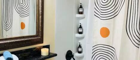 Een badkamer met een douche, toilet, wastafel en spiegel. Toiletartikelen staan op een plank en een handdoek op het aanrecht.
