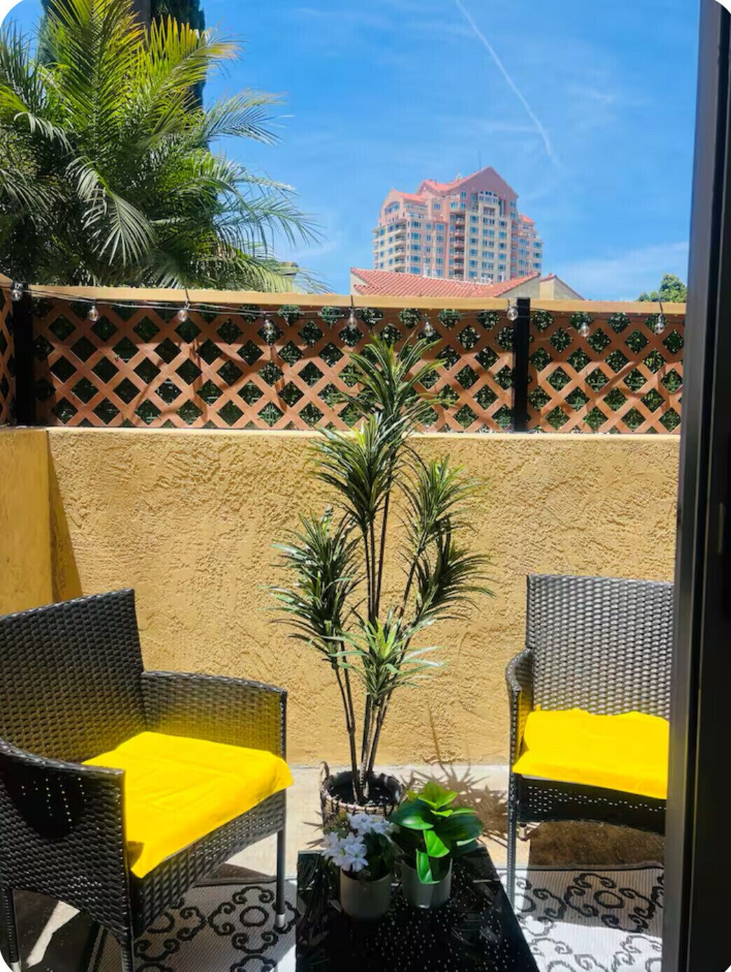 Een balkon met twee rieten stoelen, een tafeltje en een bloempot.