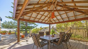 A covered outdoor patio with a wooden table and chairs, surrounded by potted plants and a hammock. - Beachside Retreat: 3  BR, 2  BA House in Lancelin, Sleeps 6 (Lancelin)