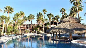 A swimming pool with palm trees and a thatched-roof structure. - Hacienda Monarcas Resort (Puerto Peñasco)