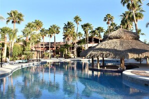 Una piscina con palme e una struttura a tetto di paglia.