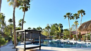 A pool area with lounge chairs, a thatched-roof structure, and palm trees. - Hacienda Monarcas Resort (Puerto Peñasco)