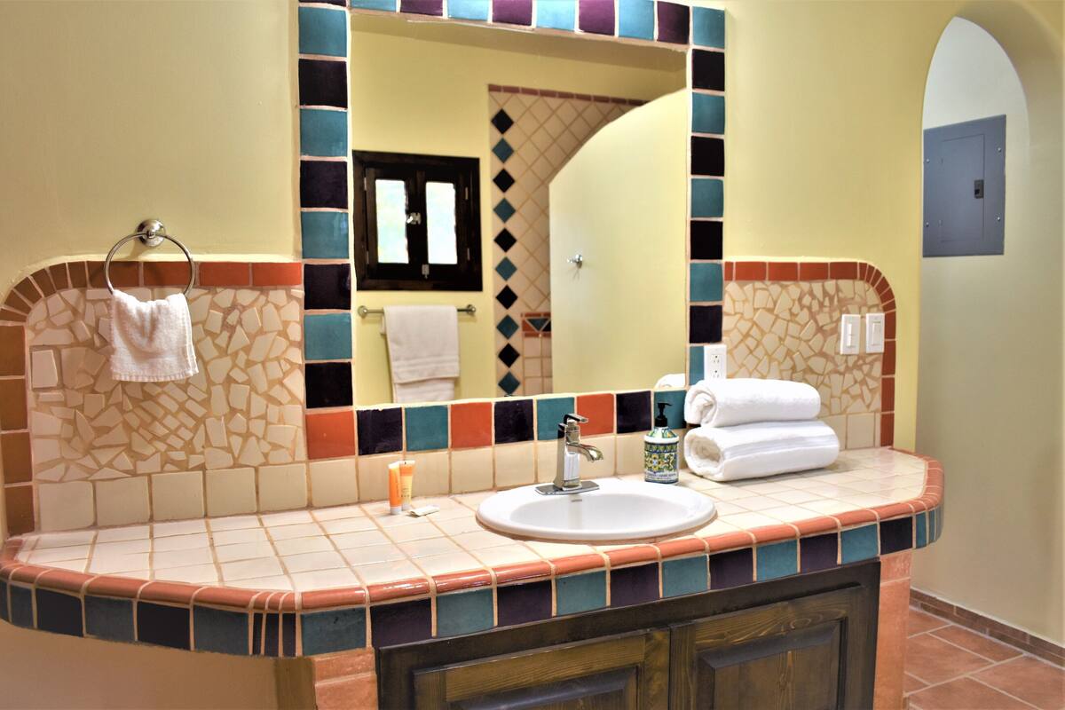A bathroom with a tiled vanity, a sink, a mirror, and a towel rack.
