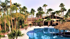A large, curved swimming pool surrounded by palm trees and a building with a tiled roof. - Hacienda Monarcas Resort (Puerto Peñasco)