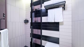 Un baño con cabina de ducha de vidrio, paredes con azulejos blancos y negros, un inodoro blanco y un perchero con una toalla blanca.