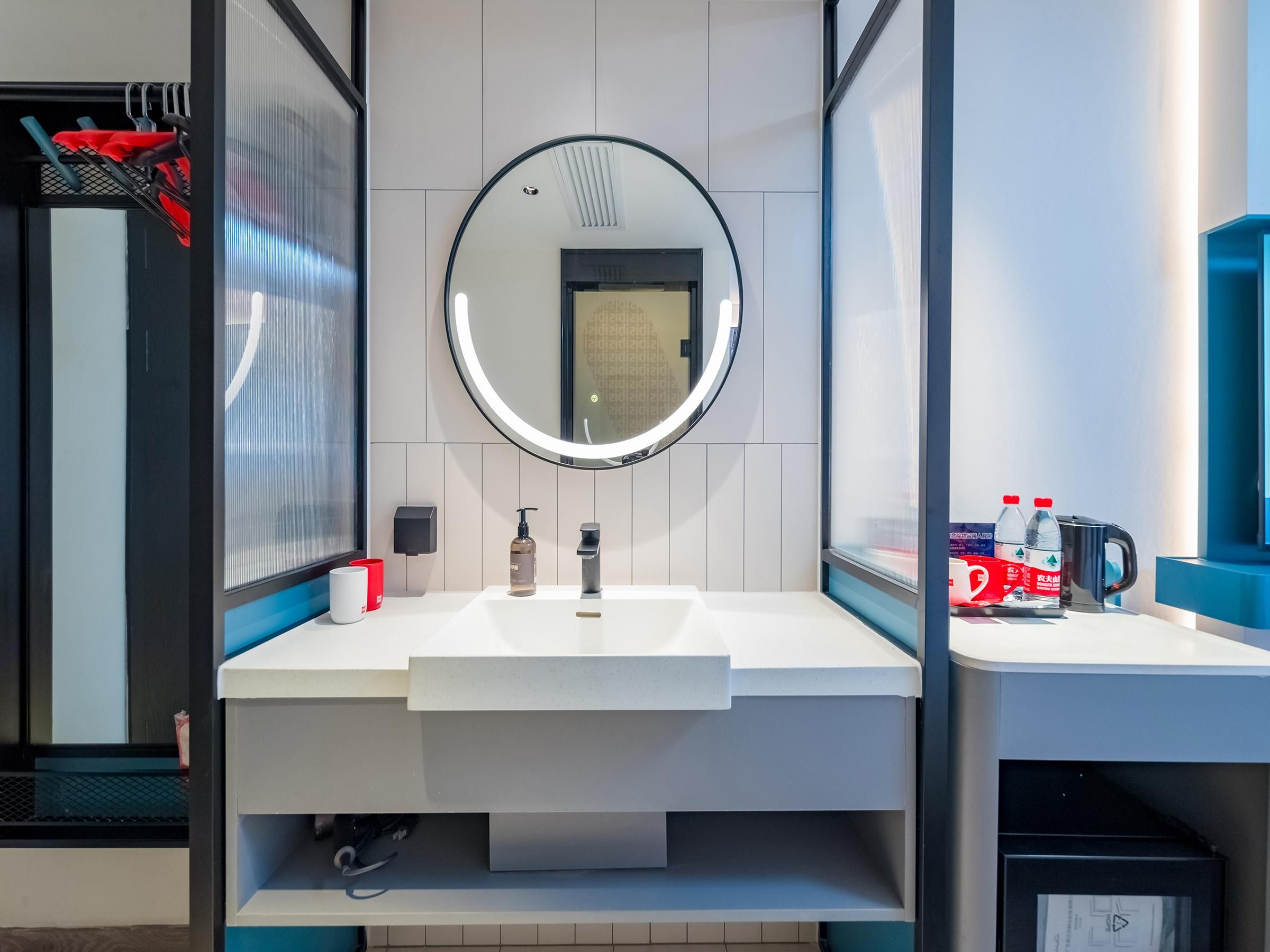 Une salle de bain moderne avec un lavabo blanc, un miroir rond, un distributeur de savon et un porte-serviettes.