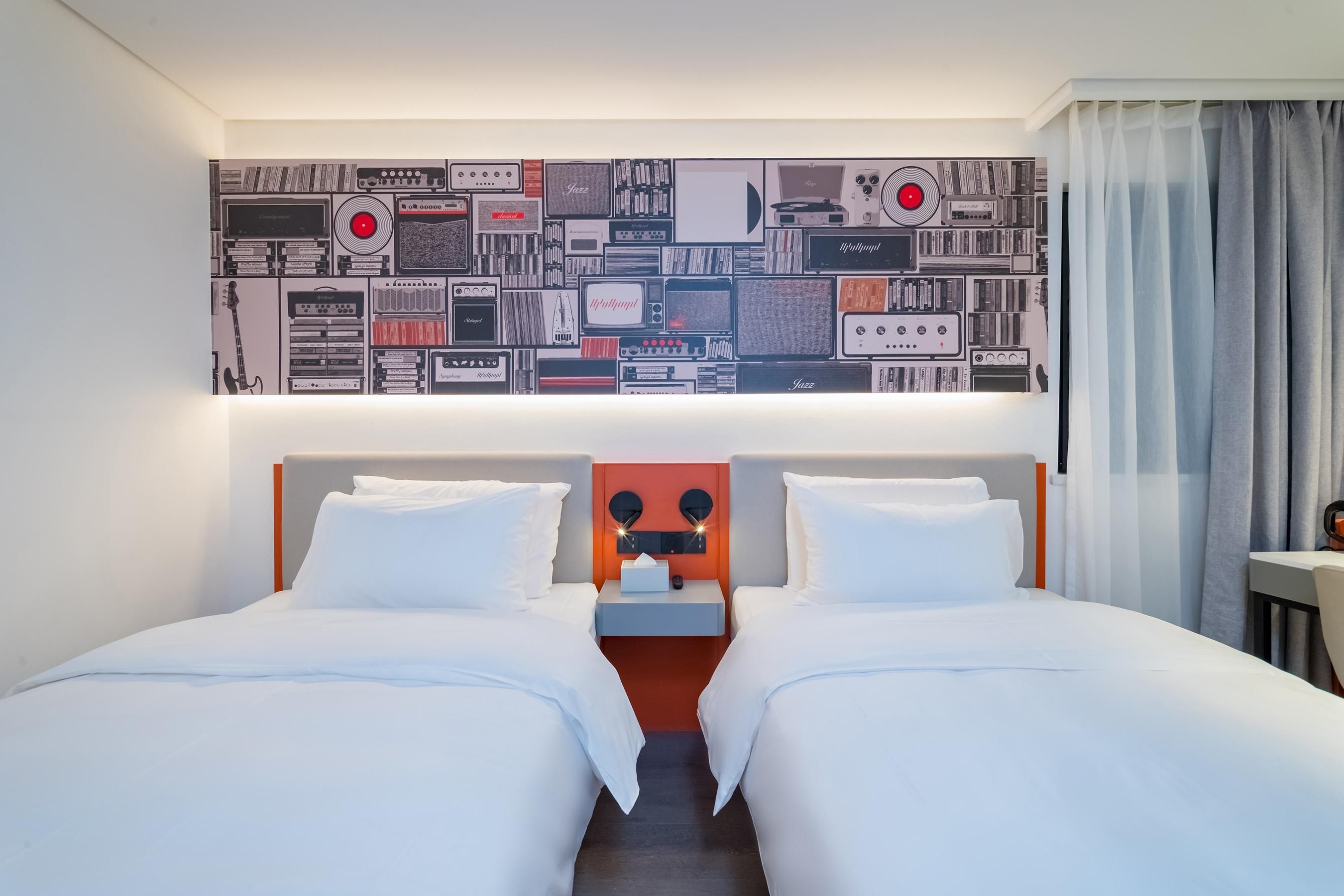 A hotel room with two beds, a headboard with a mirror, and a wall decorated with vintage audio equipment.