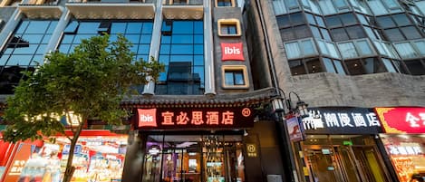 Een hotel met een moderne gevel, een opvallend ‘ibis’ bord en een traditioneel Chinees architectonisch element.