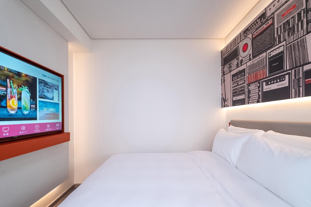 Ein Hotelzimmer mit einem Bett, einem an der Wand befestigten Fernseher, der eine Speisekarte zeigt, und einer Wand mit einem Muster aus Schwarz-Weiß-Bildern.