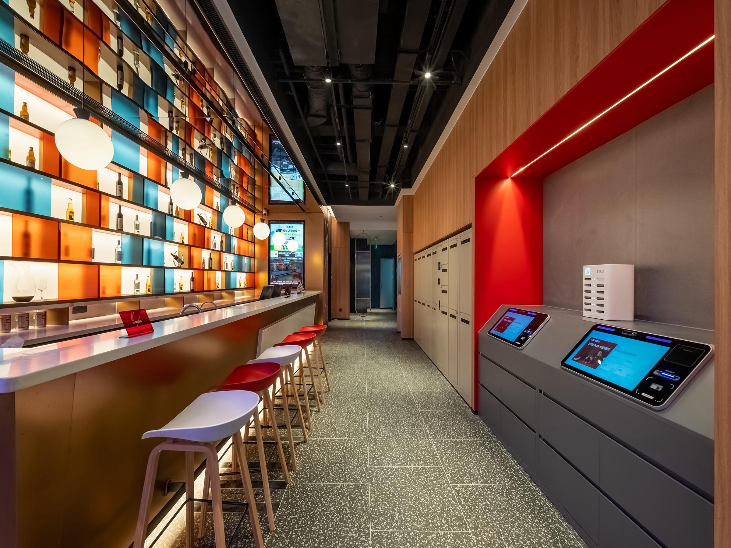 Zona de bar moderna con una barra larga, varios taburetes y una pantalla digital mostrando contenido.