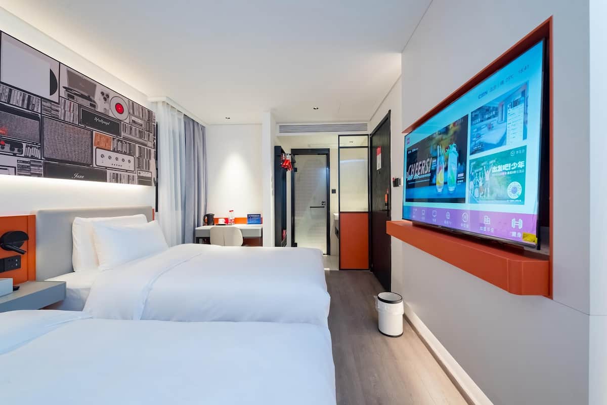 Ein Hotelzimmer mit einem großen Bett, einem Schreibtisch und einem an der Wand montierten Fernseher, der eine Speisekarte zeigt.