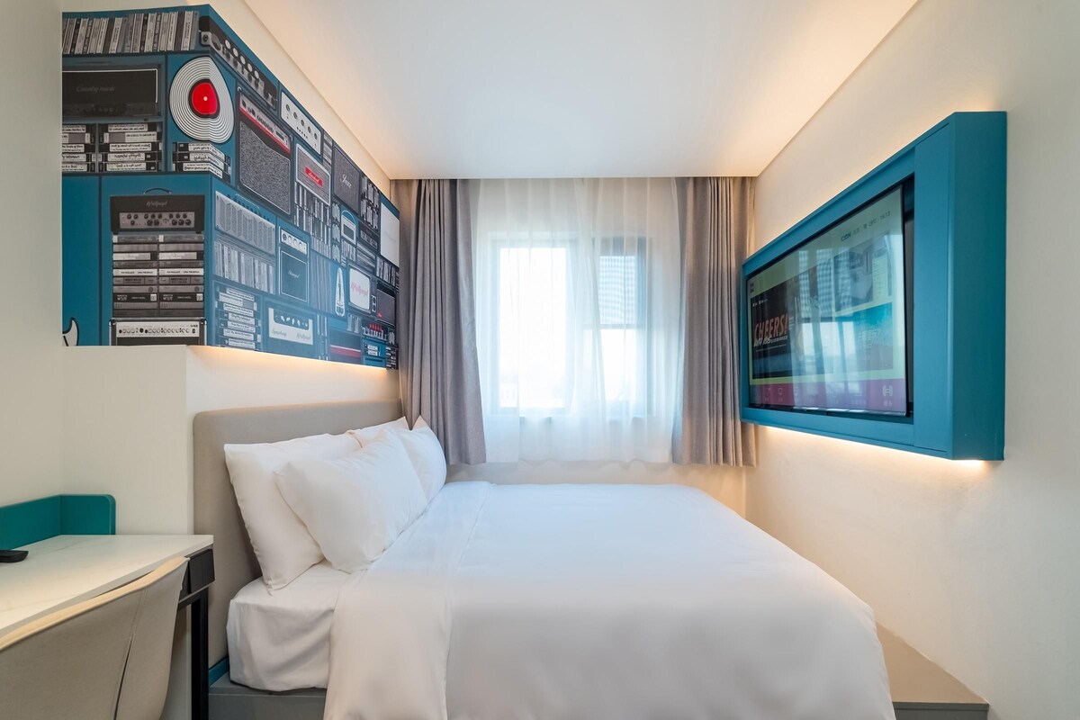 A modern hotel room with a neatly made bed, a desk, and a wall-mounted TV.