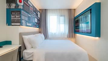A modern hotel room with a neatly made bed, a desk, and a wall-mounted TV.