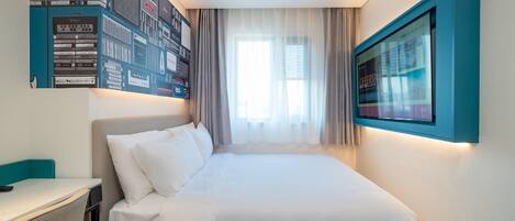 A modern hotel room with a neatly made bed, a desk, and a wall-mounted TV.
