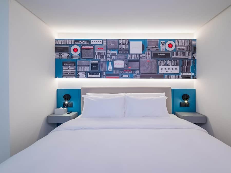 Una habitación de hotel moderna con una cama grande, dos mesitas de noche y una obra de arte en la pared que representa dispositivos electrónicos.