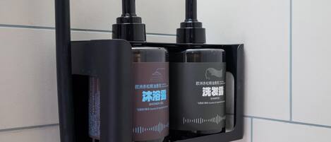 Un dispenser per sapone nero con pompa, una bottiglia marrone di gel doccia e una bottiglia nera di shampoo.