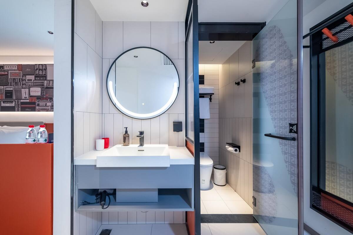 Ein modernes Badezimmer mit rundem Spiegel, weißem Waschbecken und einer Duschkabine aus Glas.