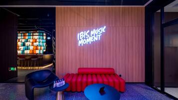 A modern lounge area with a neon sign reading "IBIS MUSIC MOMENT", a red sofa, a blue table, and a black chair.