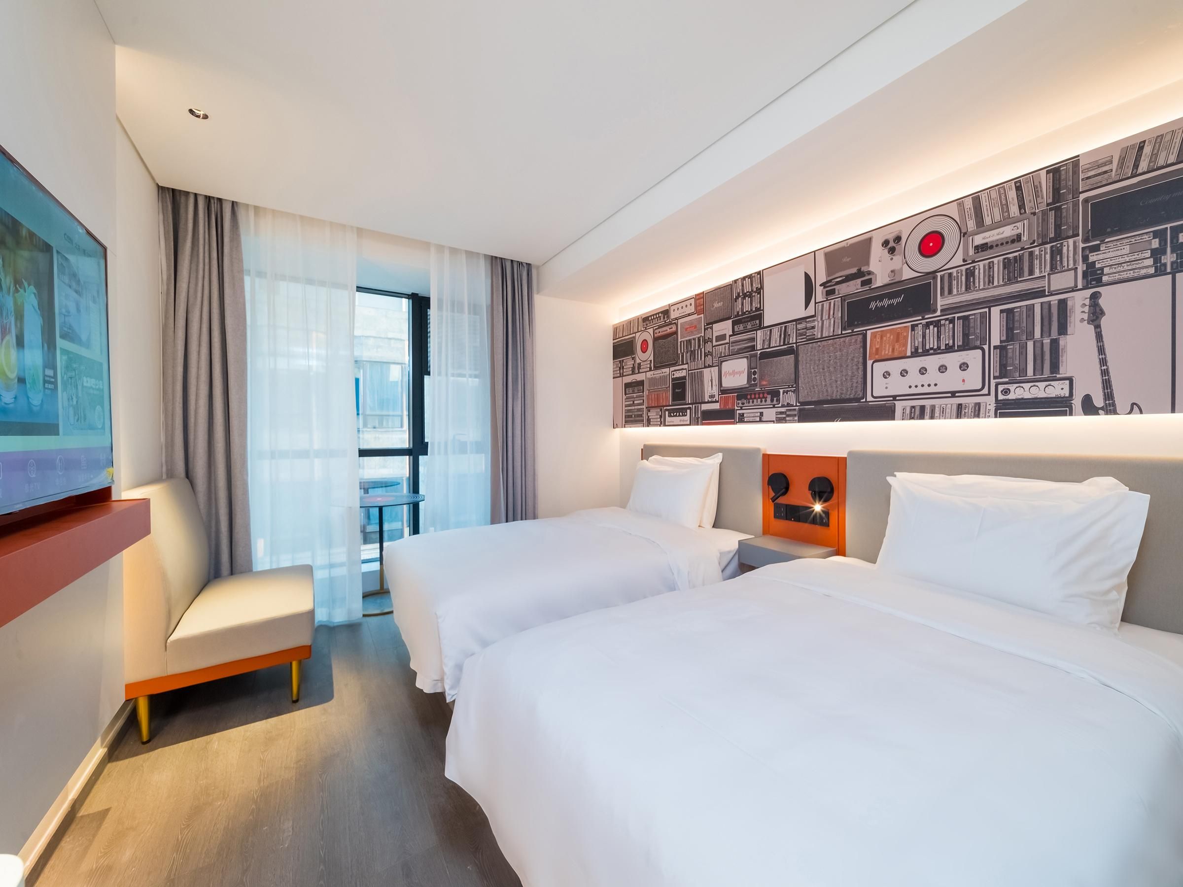 Habitación de hotel con dos camas, un televisor, una mesita pequeña y un ventanal grande con cortinas.