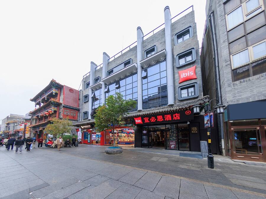Un hotel con arquitectura tradicional y moderna, un llamativo letrero rojo y una calle pavimentada frente a él.