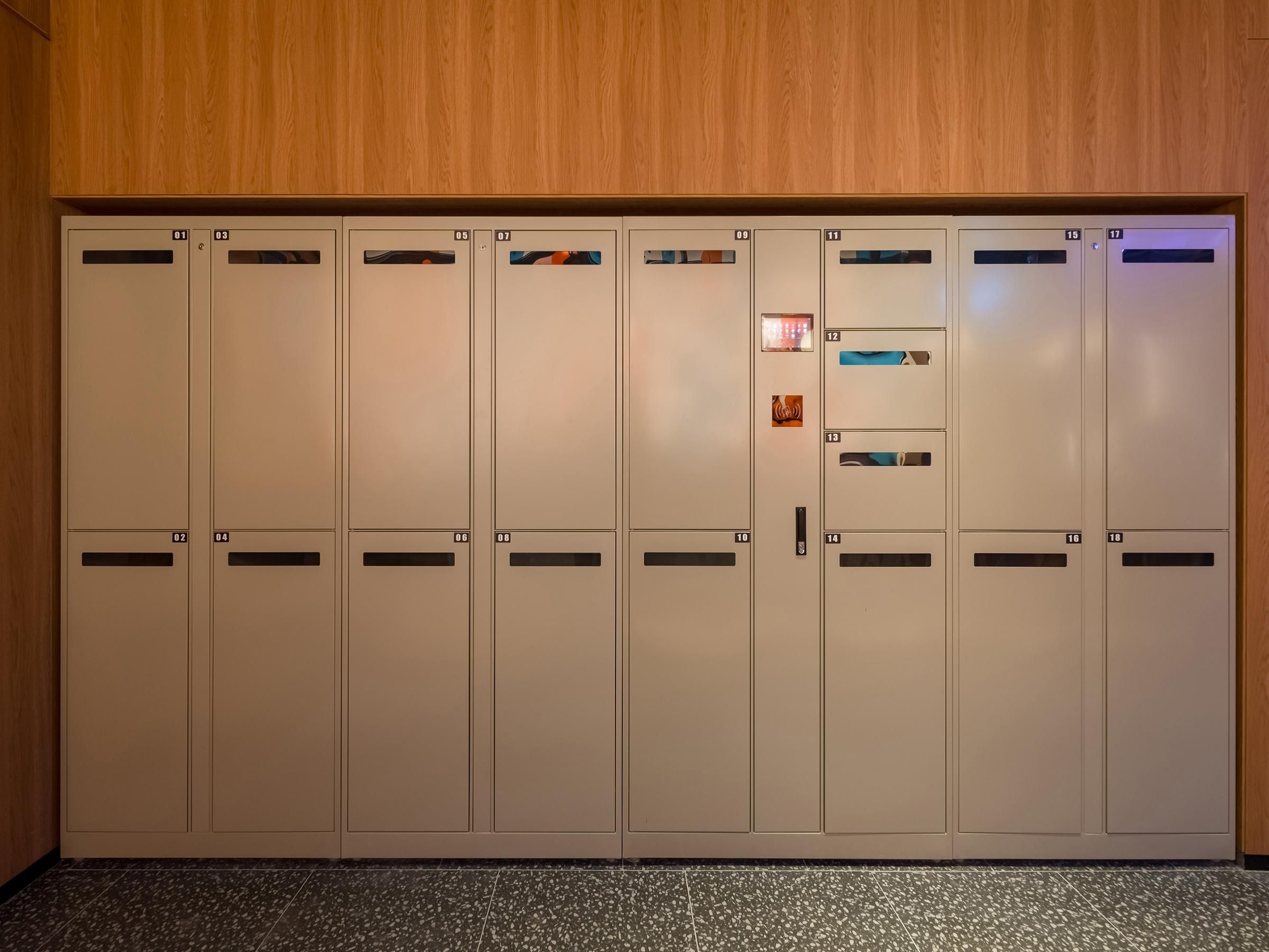 Una hilera de taquillas color beige con compartimentos numerados, una puerta central con manija y una pequeña señal iluminada arriba.