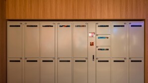 A row of beige lockers with numbered compartments, a central door with a handle, and a small illuminated sign above it. - Ibis Hotel (Beijing)