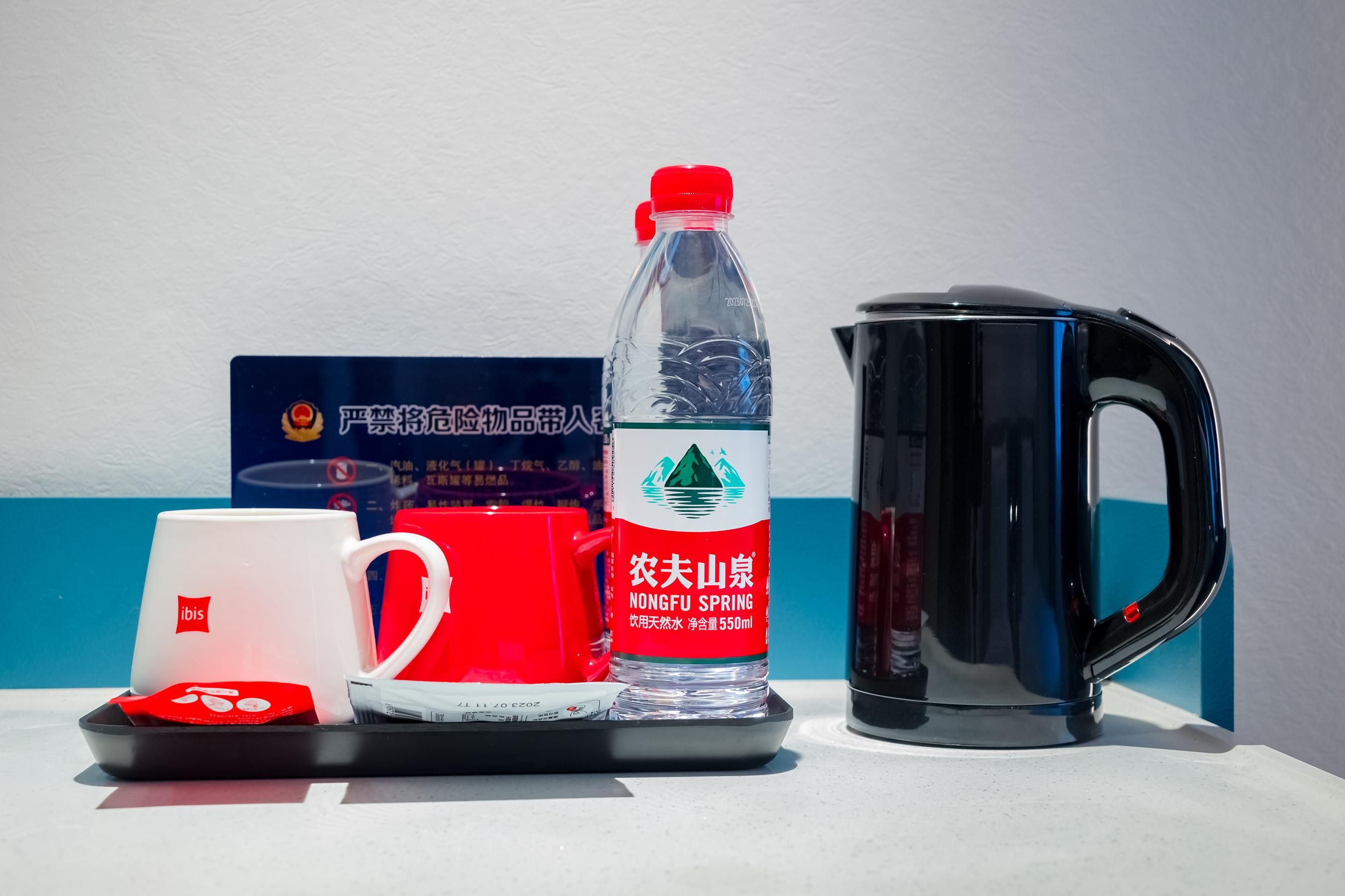 A tray with a white mug, a red mug, a clear bottle with a red cap, and a black kettle.