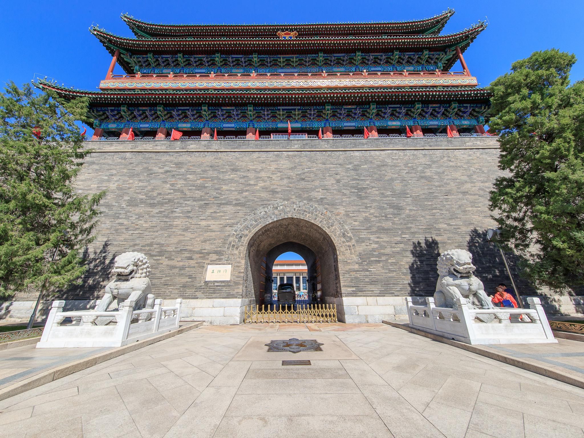 A traditional Chinese gate with ornate architecture, a stone lion statue on each side, and a clear blue sky in the background.