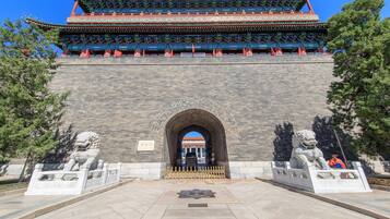 A traditional Chinese gate with ornate architecture, a stone lion statue on each side, and a clear blue sky in the background.
