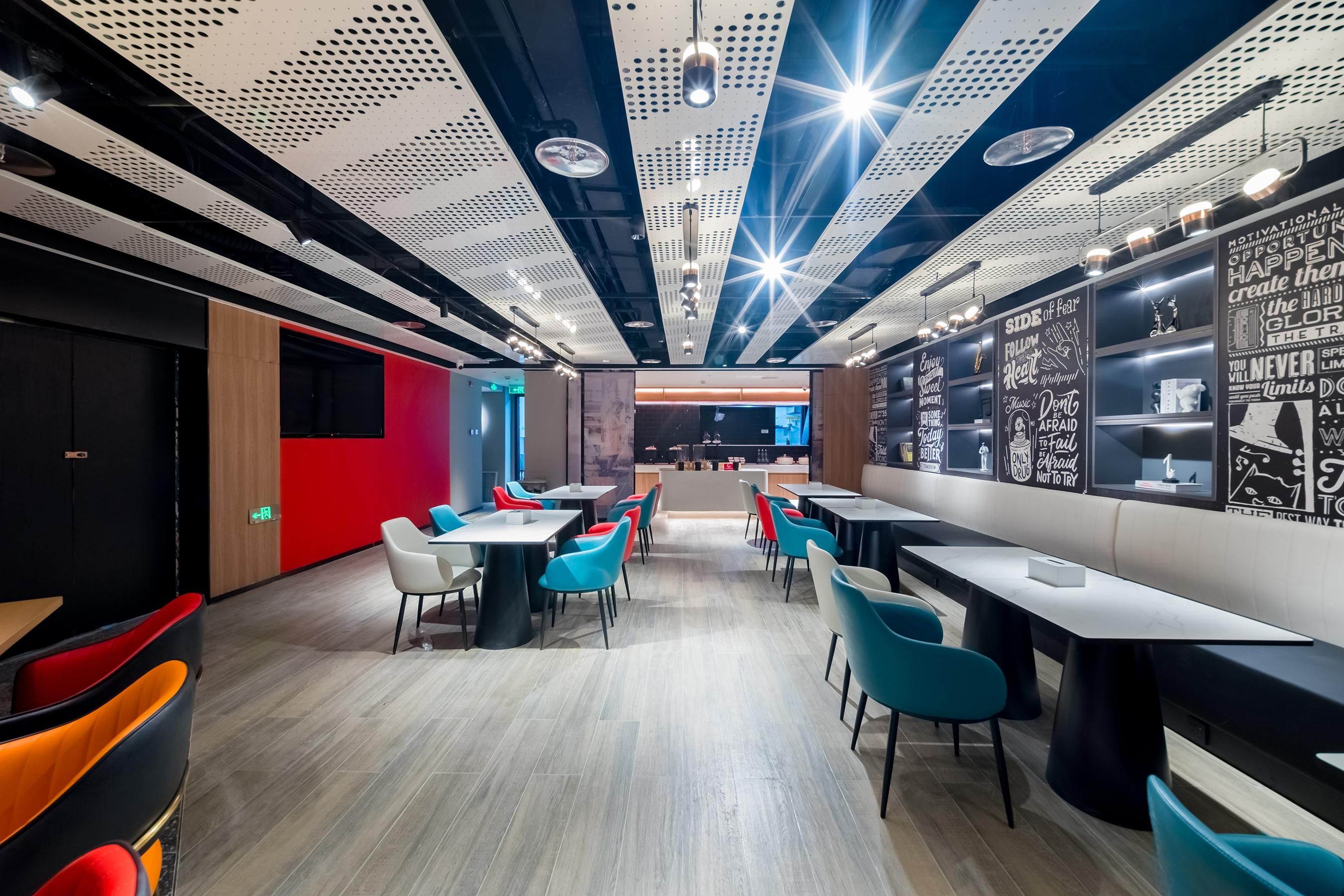 Un restaurante moderno con techos altos, paneles perforados y arte mural inspirador. Mesas y sillas dispuestas para comer.