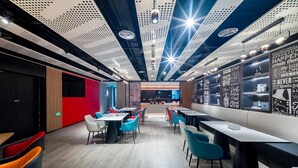A modern restaurant with a high ceiling, perforated panels, and motivational wall art. Tables and chairs are arranged for dining. - Ibis Hotel (Beijing)