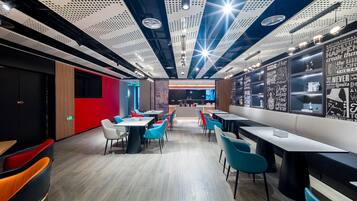 Un restaurante moderno con techos altos, paneles perforados y arte mural inspirador. Mesas y sillas dispuestas para comer.