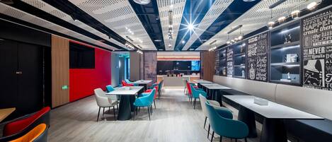 A modern restaurant with a high ceiling, perforated panels, and motivational wall art. Tables and chairs are arranged for dining.