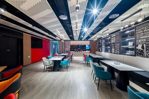 A modern restaurant with a high ceiling, perforated panels, and motivational wall art. Tables and chairs are arranged for dining. - Ibis Hotel (Beijing)