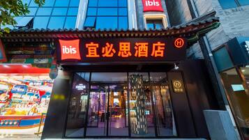 Entrada de un hotel con estilo arquitectónico chino tradicional, fachada de vidrio moderna y un letrero llamativo de 'ibis'.