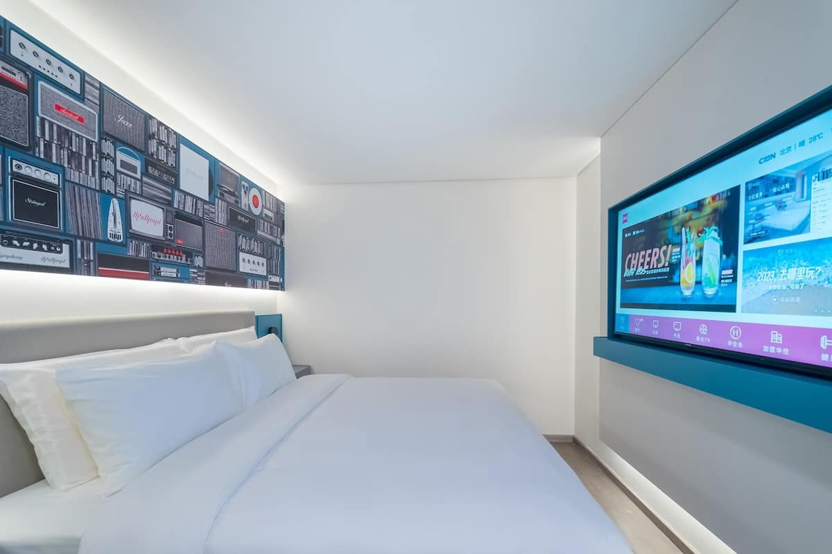Ein modernes Hotelzimmer mit einem großen Bett, einem an der Wand befestigten Fernseher und einer Wand, die mit alten Radios und Fernsehgeräten dekoriert ist.