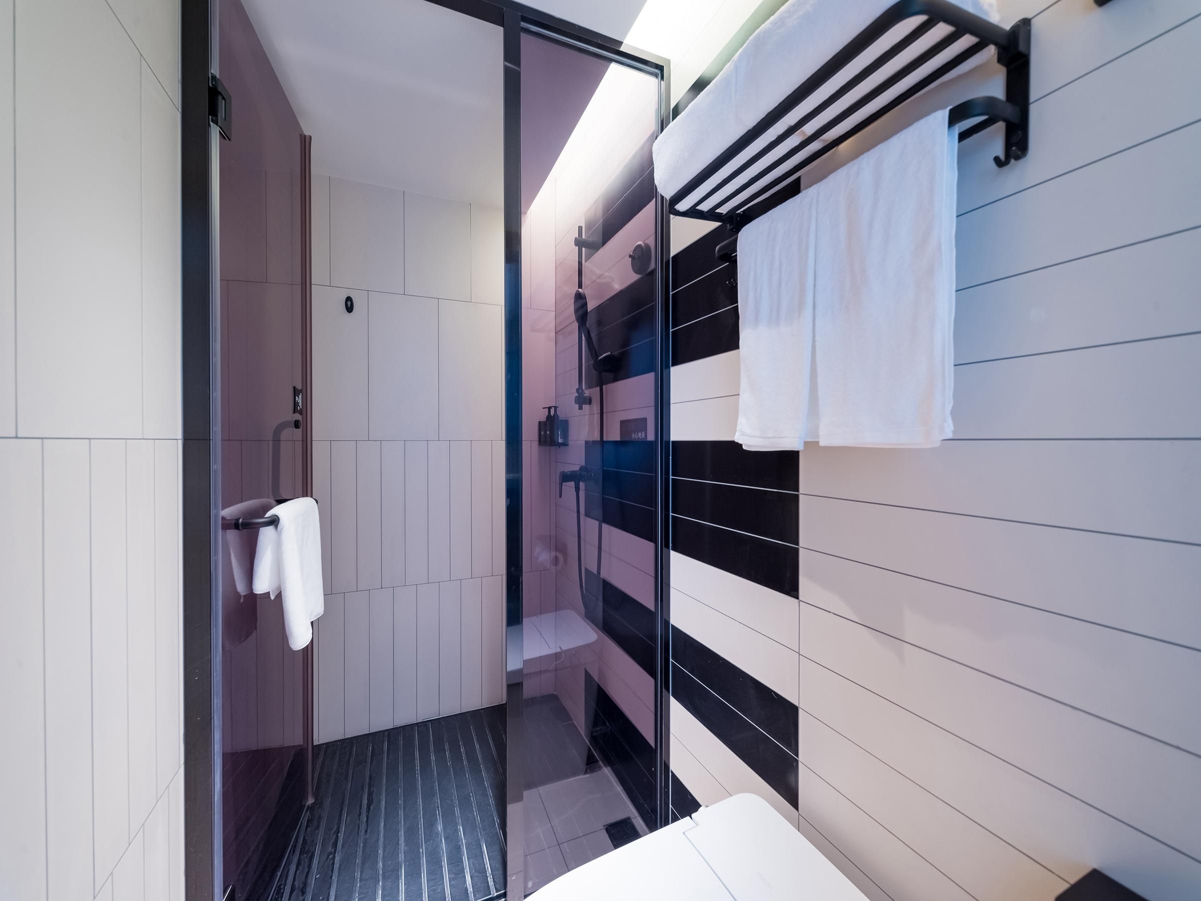 Un baño moderno con cabina de ducha de vidrio, pared con azulejos blanco y negro y un perchero con dos toallas blancas.